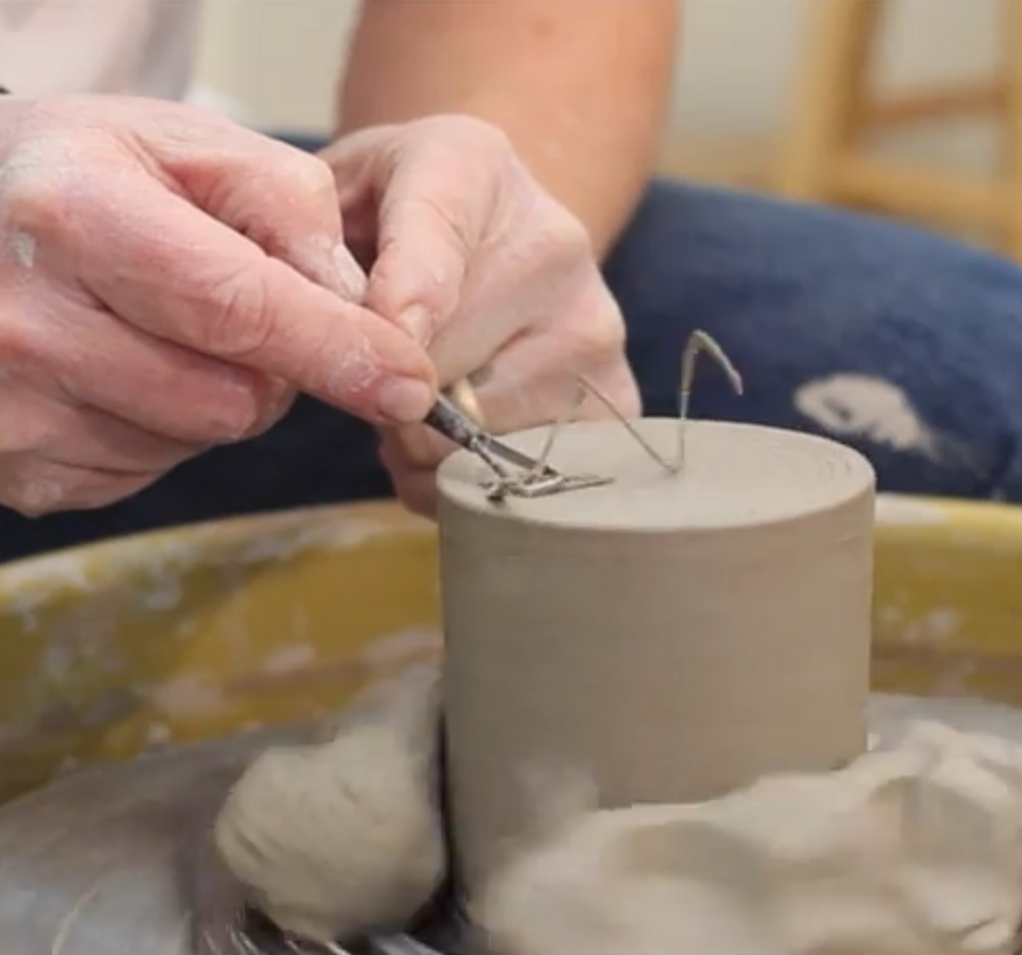 John Britt trims the bottom of a spinning grey ceramic cup, a clay shaving spiraling off.