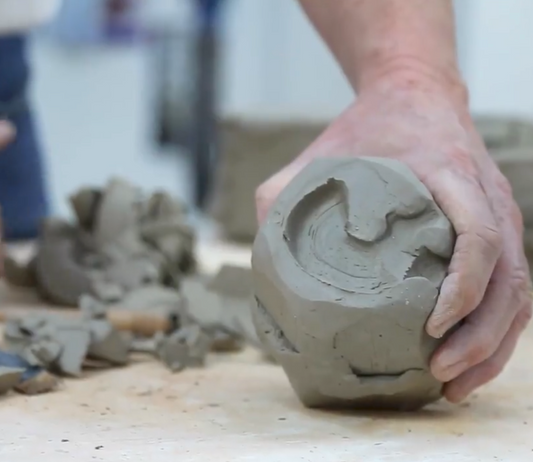 Hand holding a clay sculpture on a workbench with clay pieces and tools in the background