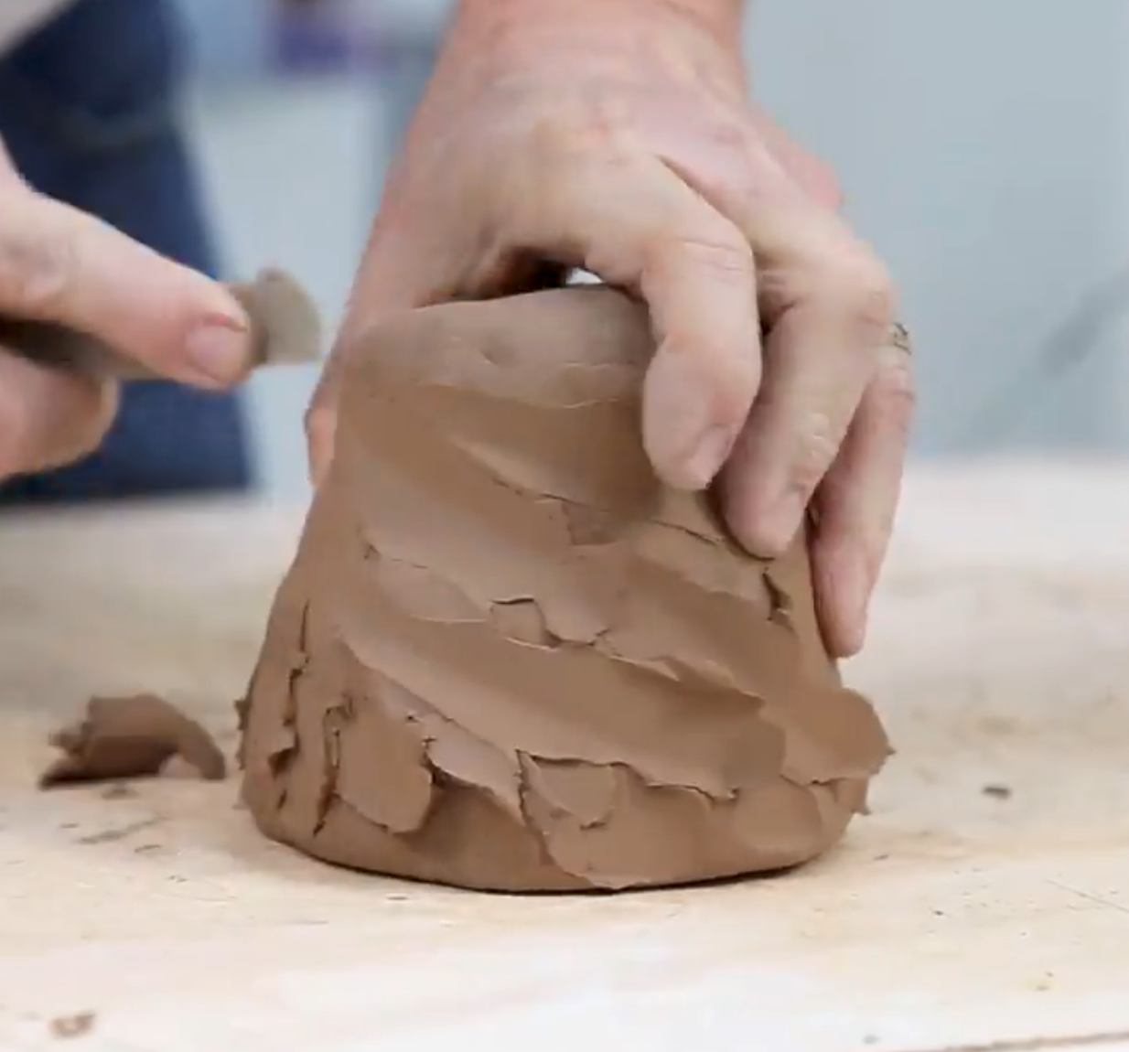 Hands in motion shaping a clay pot on a wooden surface