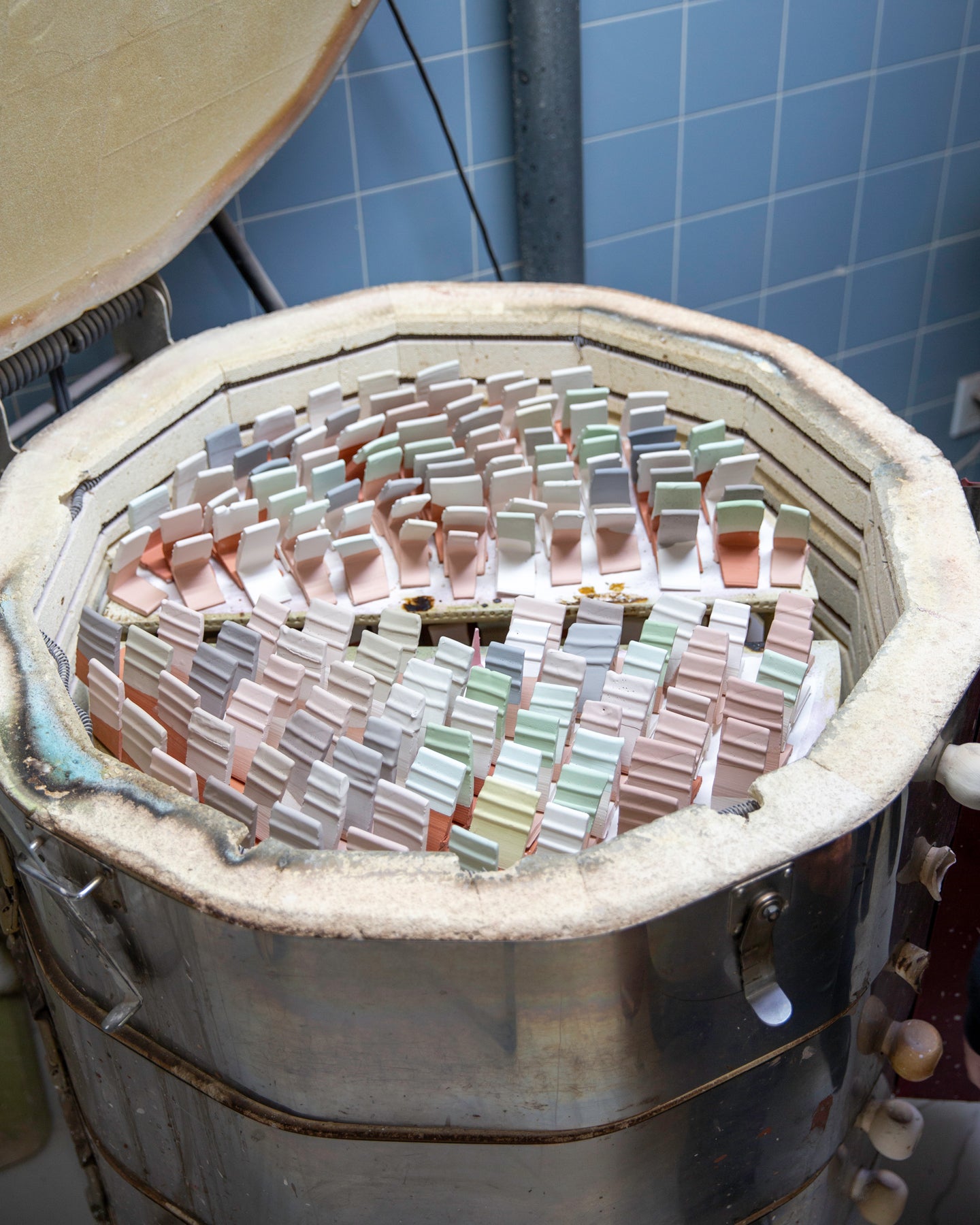 Colorful ceramic test tiles inside a kiln with blue tiled wall in the background