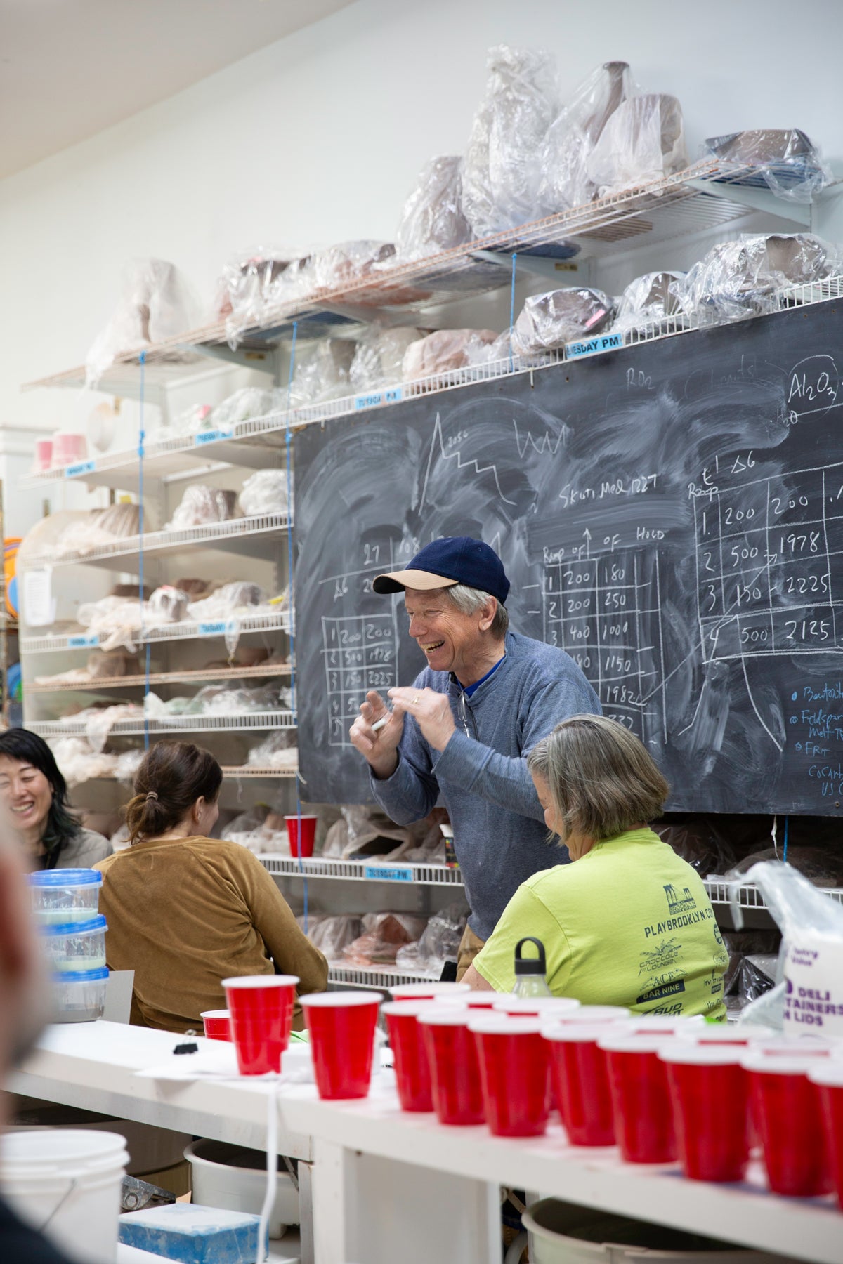 Group of people in a workshop setting with red cups on a table and a chalkboard in the background. John britt is gesturing and smiling in front of the chalkboard