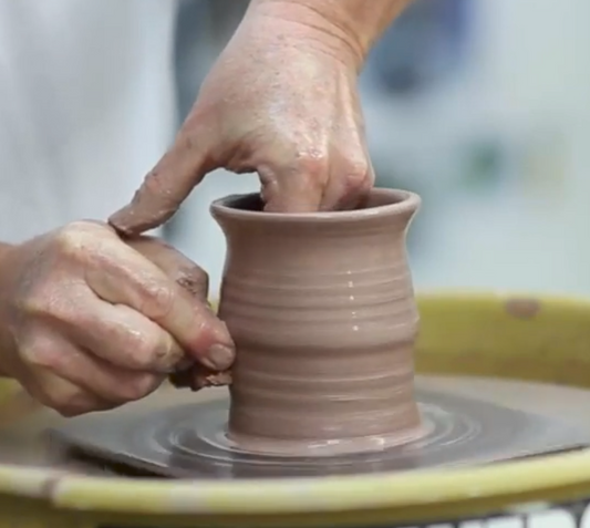 A close up of artist John Britt shaping a clay pot on a pottery wheel in his NC studio.