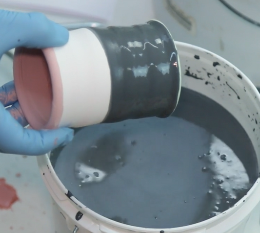 A closeup of John Britt's gloved hand pouring dark liquid from a container into a white bucket.