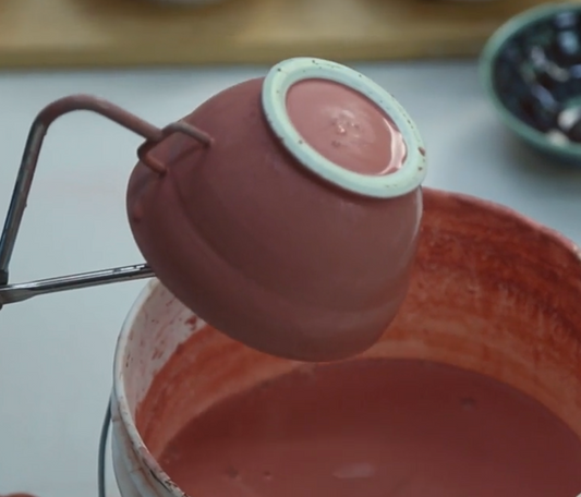 A view inside John Britt's studio: a pink ceramic pot, held with tongs, is being pulled out a bucket filled with pink liquid