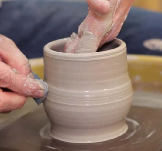 A close up of potter John Britt's hands as he spins a wet clay pot on the pottery wheel. 