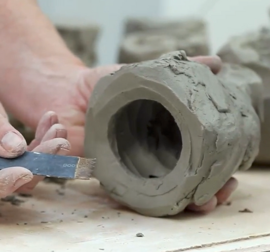 Close up of a person working with clay on a wooden surface